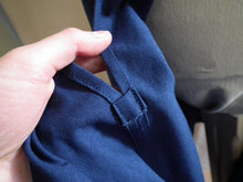 Load image into Gallery viewer, A close up of the side slit of the dark royal blue Europaea skirt. A hand holds the slit toward the camera to show the reinforcement patch at the bottom of the slit.