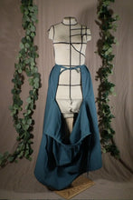 Load image into Gallery viewer, The open front view of an ankle-length forest green skirt in a crisp woven fabric, with pleats at the narrow waistband, on a dressform in a studio. The front part of the skirt has fallen open to reveal the waist ties from the back portion of the skirt, the back ties are knotted at the waist. There are some fake green vines in the background.