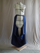 Load image into Gallery viewer, The open front view of an ankle-length dark royal blue skirt in a crisp woven fabric, with pleats at the narrow waistband, on a dressform in a studio. The front part of the skirt has fallen open to reveal the waist ties from the back portion of the skirt, the back ties are knotted at the waist.
