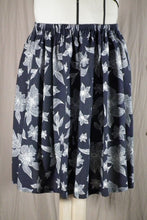 Load image into Gallery viewer, A close up on the Cordata skirt, a short knee-length elastic waistband skirt in a drapey rayon print that's dark blue with white flowers. It's displayed on a dress form, showing the front view.