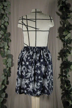 Load image into Gallery viewer, Closer back view of a short knee-length elastic waistband skirt in a drapey rayon print that's dark blue with white flowers. It's displayed on a dress form. In the background are some fake green vines.