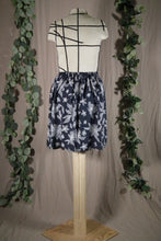 Load image into Gallery viewer, back view of a short knee-length elastic waistband skirt in a drapey rayon print that's dark blue with white flowers. It's displayed on a dress form. In the background are some fake green vines.