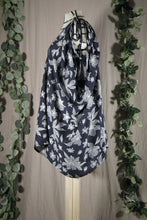 Load image into Gallery viewer, A long pleated skirt in a drapey rayon print that's dark blue with white flowers is displayed on a dress form as a swim coverup, showing the side view. The waist ties are knotted at the shoulder, forming a bow, and elegant draping around the armscye. In the background are some fake green vines.