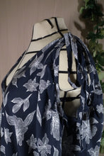 Load image into Gallery viewer, A closer ¾ front view of drapey rayon print skirt that's dark blue with white flowers, displayed on a dress form as a swim coverup. The slit makes a deep V at the neck, and ties make drapey bows at the shoulder. In the background are some fake green vines.