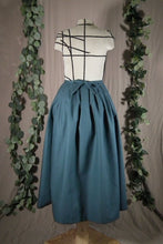 Load image into Gallery viewer, The back view of an ankle-length forest green skirt in a crisp woven fabric, with pleats at the narrow waistband, on a dressform in a studio, with some fake green vines in the background. There&#39;s a bow made from the waist ties at the centre back.
