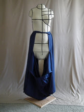 Load image into Gallery viewer, The open front view of an ankle-length dark royal blue skirt in a crisp woven fabric, with pleats at the narrow waistband, on a dressform in a studio. The front part of the skirt has fallen open to reveal the waist ties from the back portion of the skirt, the back ties are knotted at the waist.
