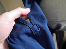 Load image into Gallery viewer, A close up of the side slit of the dark royal blue Europaea skirt. A hand holds the slit toward the camera to show the reinforcement patch at the bottom of the slit. 
